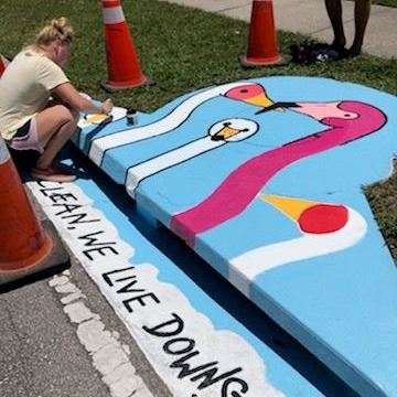 Artist Mary Compton painting the storm drain on Michigan Avenue as part of the storm drain community